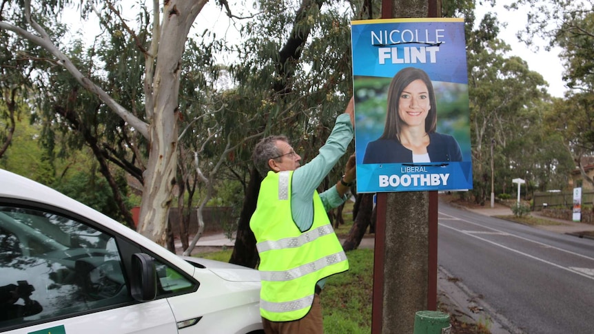 A council worker removes a campaign poster promoting the Liberal candidate for Boothby.