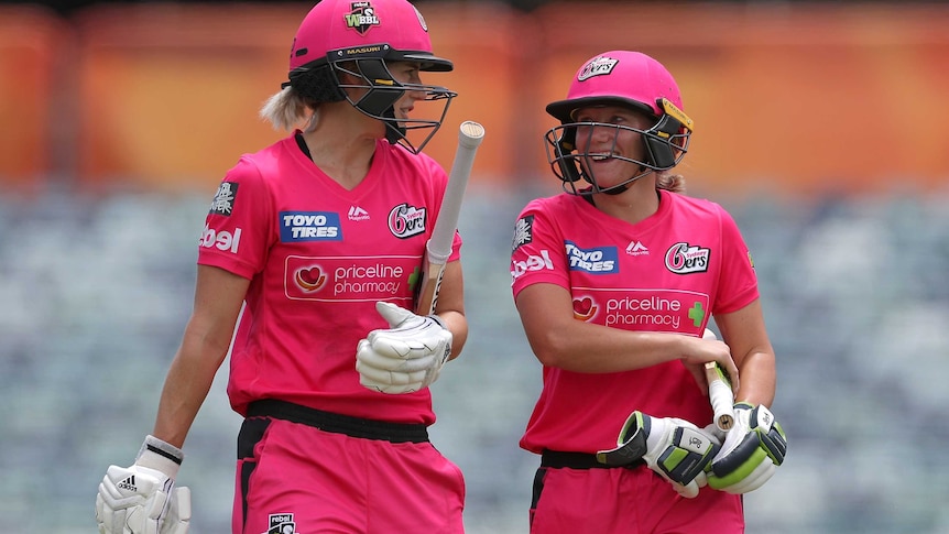 Wearing helmets and carrying their bats, Perry and Healy look at each other and smile as they walk off the field