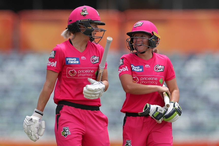 Wearing helmets and carrying their bats, Perry and Healy look at each other and smile as they walk off the field