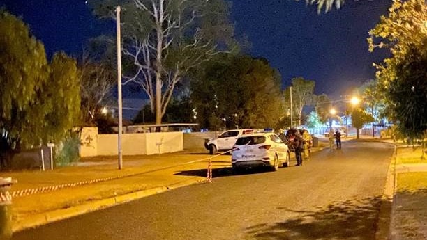 A crime scene on a suburban Alice Springs street is flanked by police cars and officers.