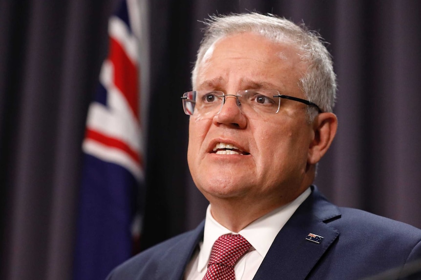 Mr Morrison is standing behind a lectern with an Australian flag in the background. He's mid sentence.
