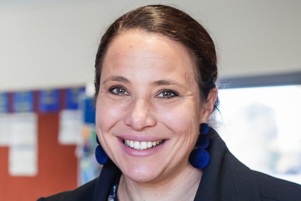 Close up shot of brunette woman smiling open mouthed smile, wearing blue earrings and jacket