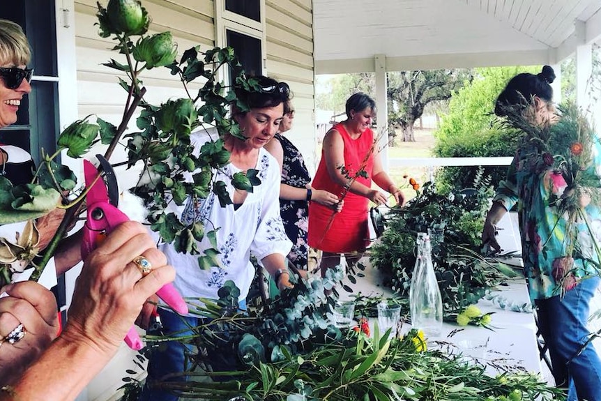 ladies standing around a table of flowers making arrangements on a homestead verandah