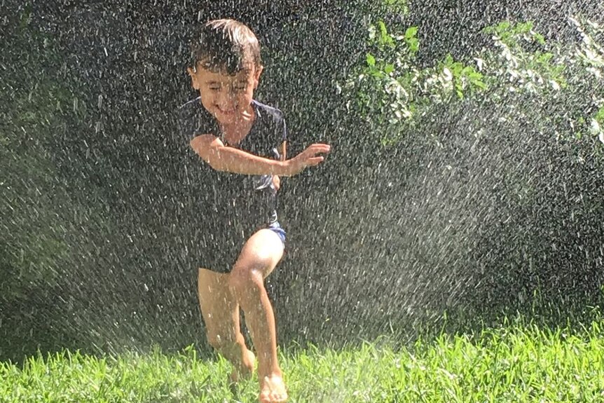 A child plays in the sprinkler