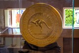 A giant gold coin with a kangaroo on the front inside a glass case.