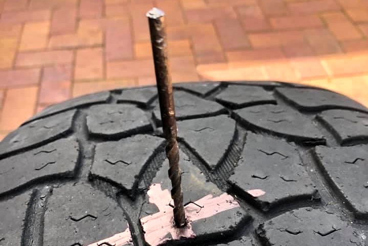 A steel rod sticks out of a car tyre with a pink X marking the spot it entered.