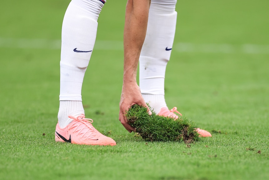 A picture of a player's legs as they stand on the pitch during a EURO 2024 game holding a big piece of grass and turf.