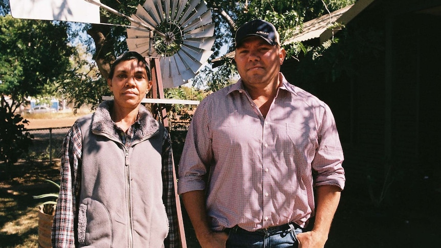 A woman and her brother look at the camera while standing in front of a windmill.