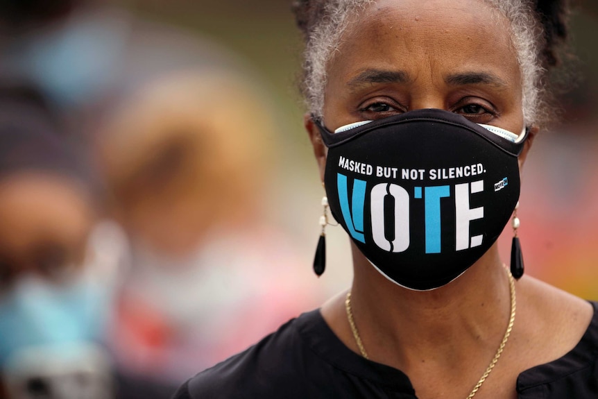 An African American woman in a face mask with 'masked but not silent, vote' written on it