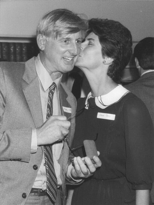 A man hugs a woman while holding a small medal.