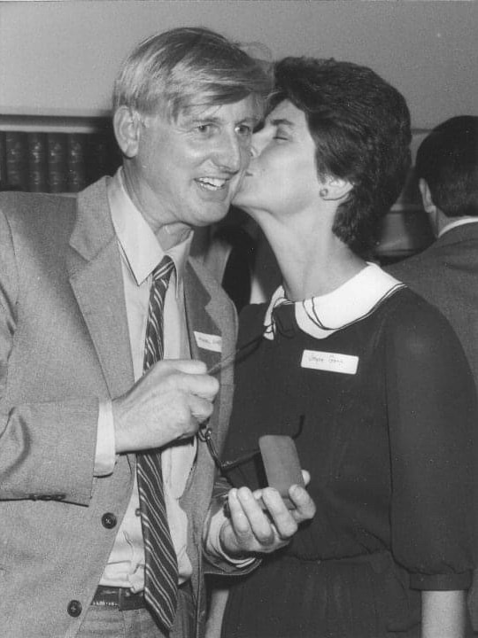 A man hugs a woman while holding a small medal.