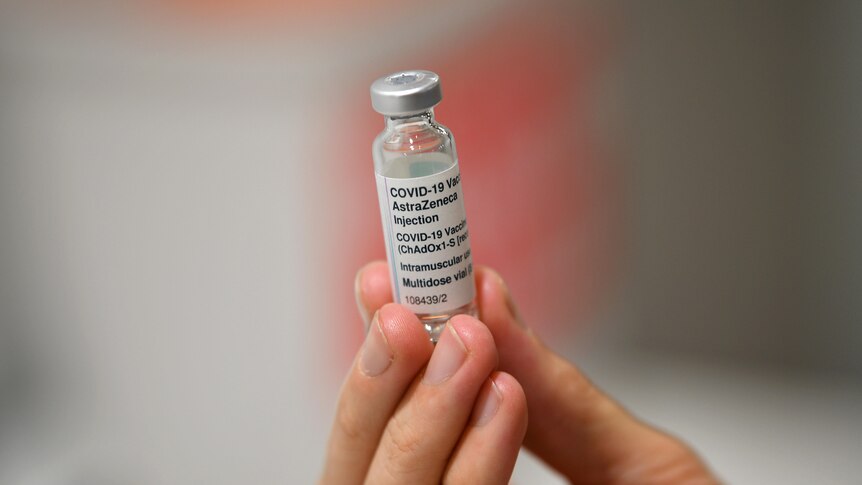 A hand holding a vaccine vial. AstraZeneca 5ml is printed on the label