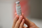 A close-up of a person holding up a vial of the AstraZeneca vaccine.