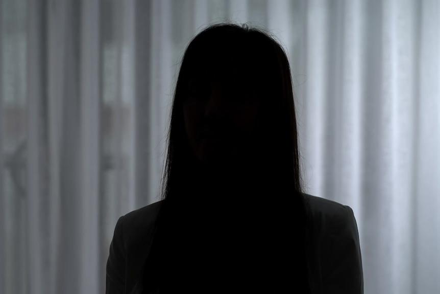 The darkened silhouette of a woman with straight long hair against a non-descript white curtain.