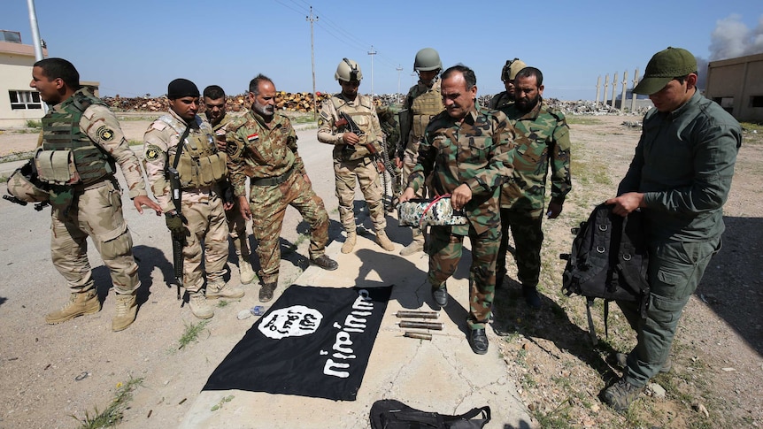 Iraqi soldiers lay an Islamic State flag on the ground.