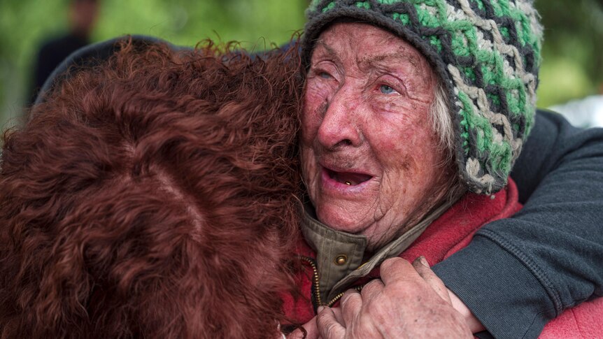 A close-up of an old woman crying while being hugged by another woman. 