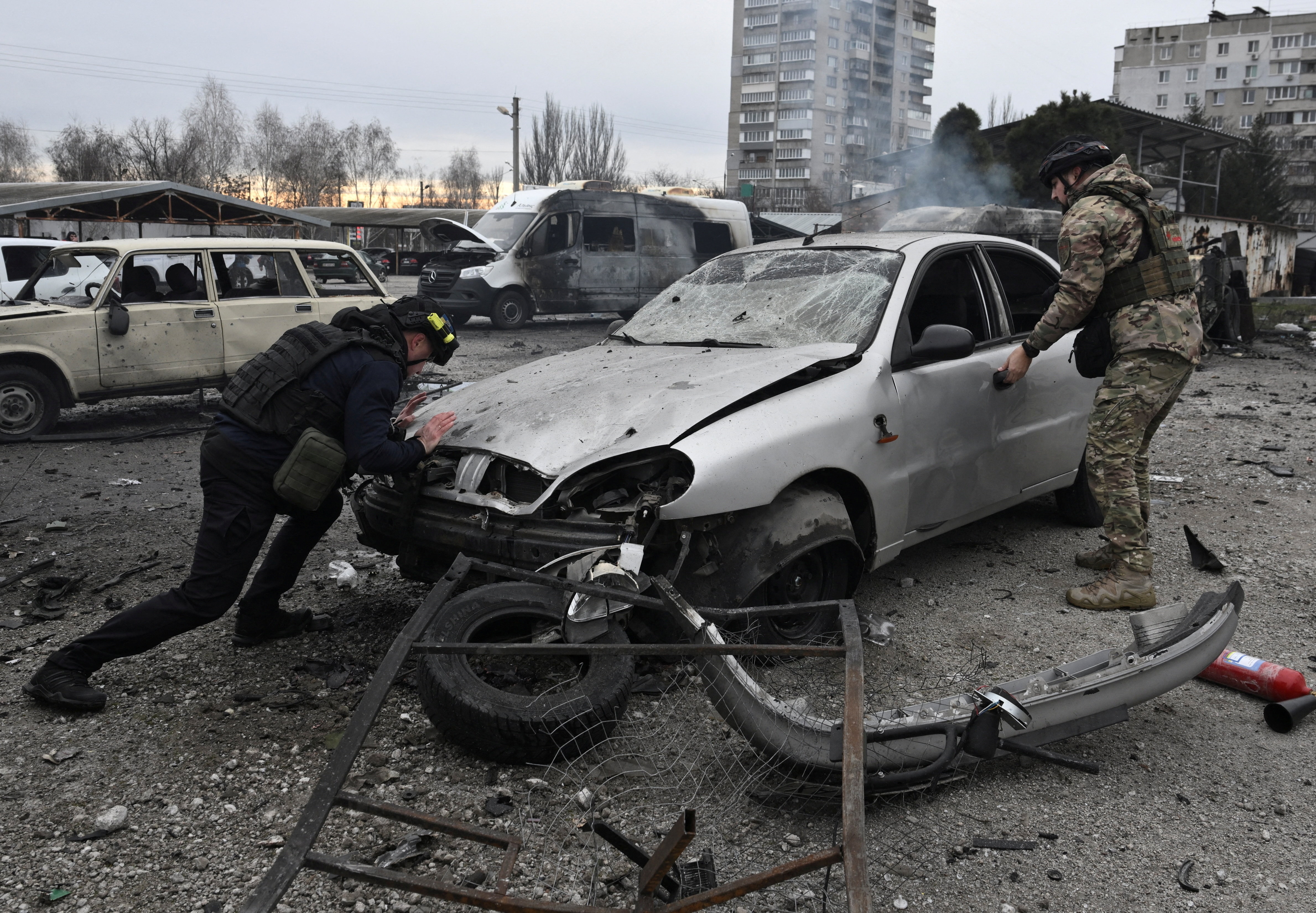 A police officer trying to push a car which has been damaged in a drone strike.
