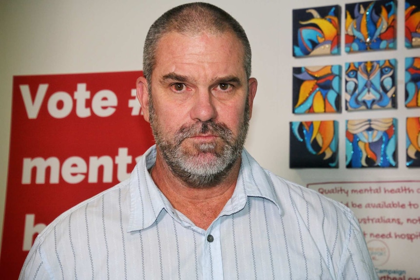 A man wearing a blue collared shirt looks into the camera