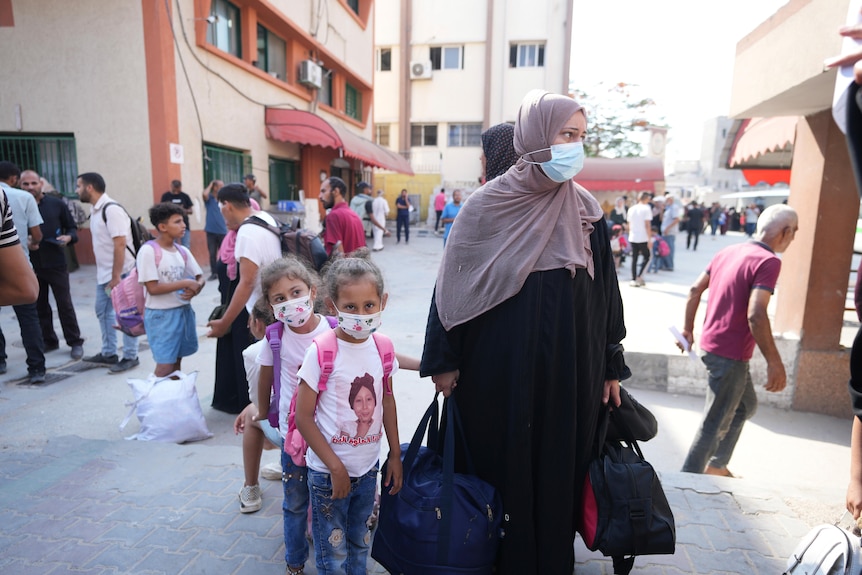 Palestinian children wearing masks stand next to their mother