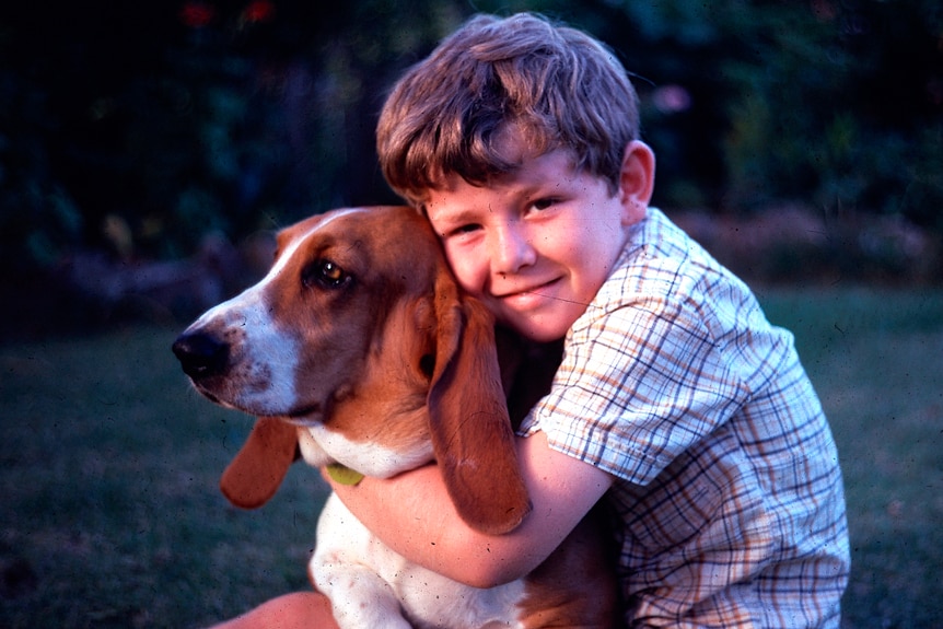 A young boy hugs a basset hound on a lawn