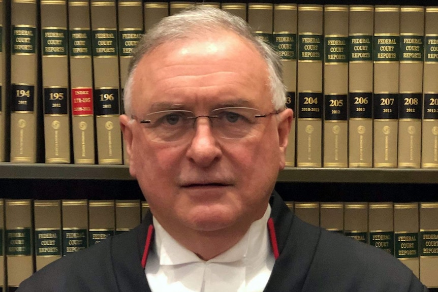 Justice Kevin Bell standing in front of a bookcase.