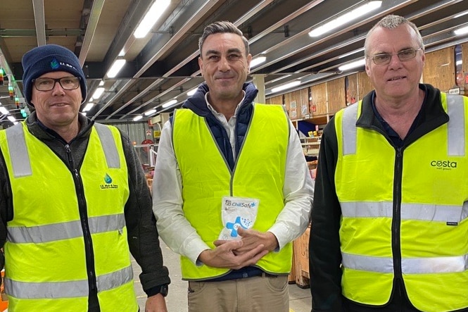 Trois hommes en haute visibilité souriant à l'intérieur d'un entrepôt