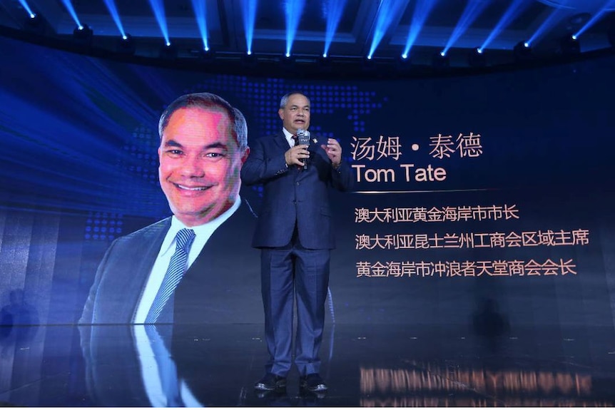 Tom Tate stands in front of a banner featuring his photo and name.