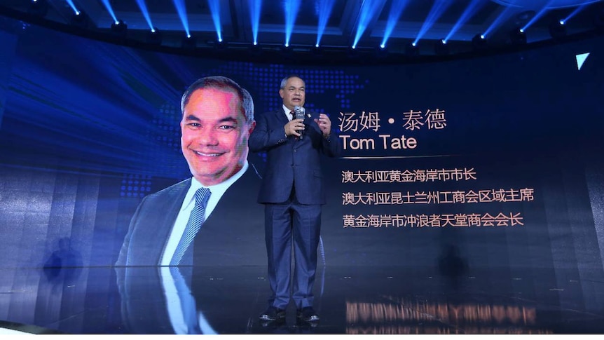 Tom Tate stands in front of a banner featuring his photo and name at the Beijing project launch.