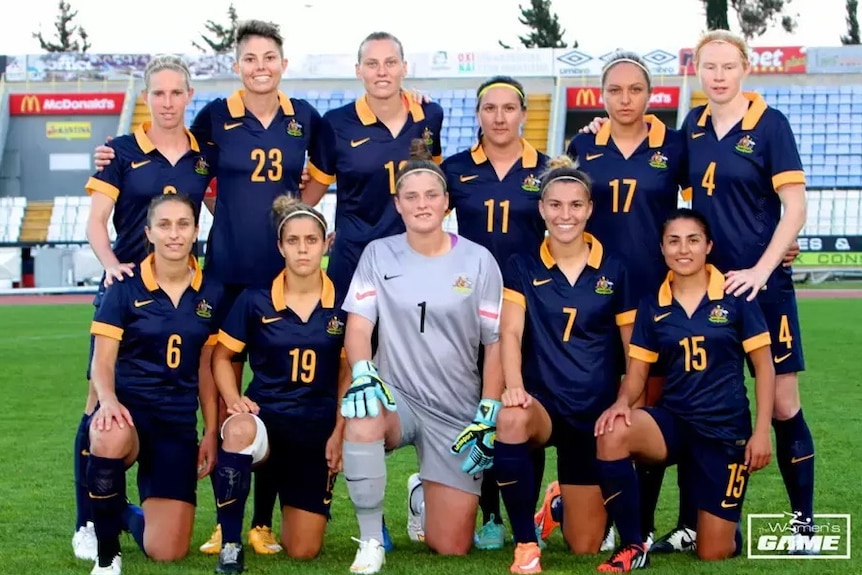 A women's soccer team wearing blue and yellow poses for a photo before a game