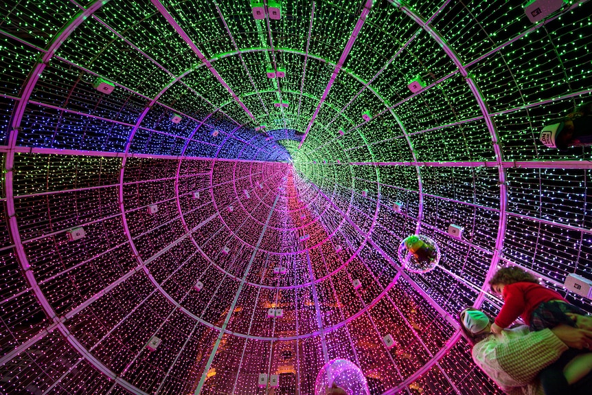a Christmas tree made of lights of different colors can be seen from below as well as a woman holding a child below