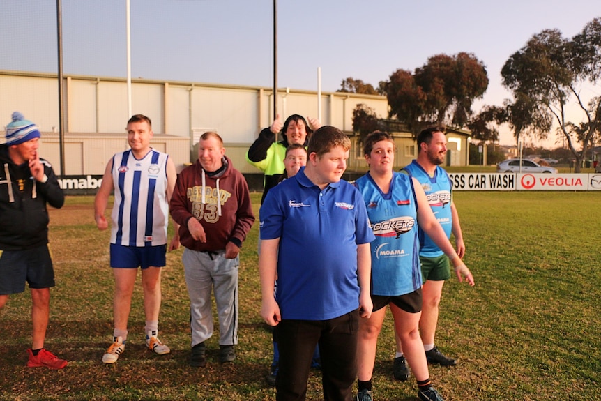 A group of eight Rockets team members standing near a footy goal, basked in golden light from the sunset.