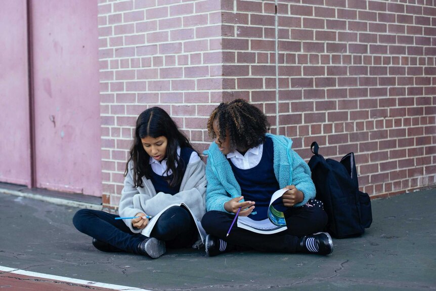 Two school girls sit looking at books
