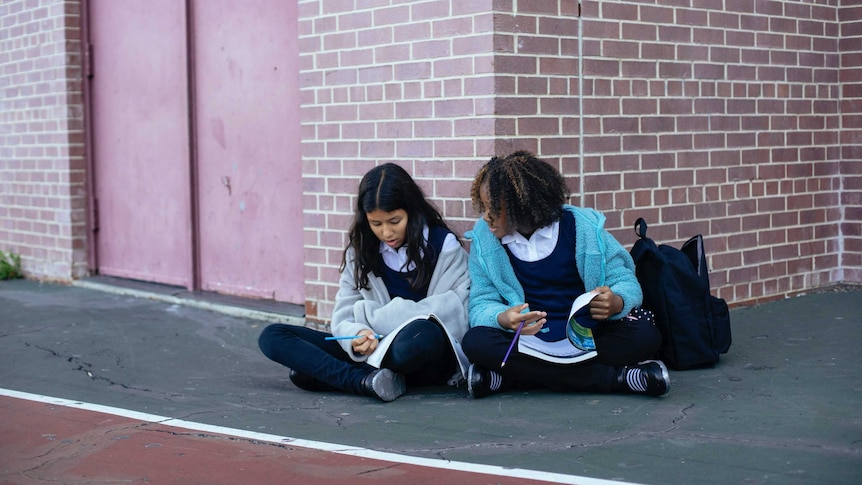 Two school girls sit looking at books in a story about how to help your child make friends in school.