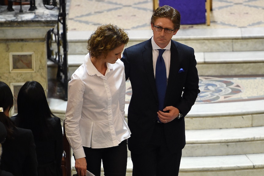 a man wearing glasses holding the arm of a woman at a church service