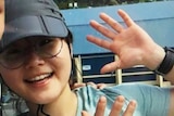 Joohee Han smiles and waves in a selfie, wearing a cap and glasses, date unknown.