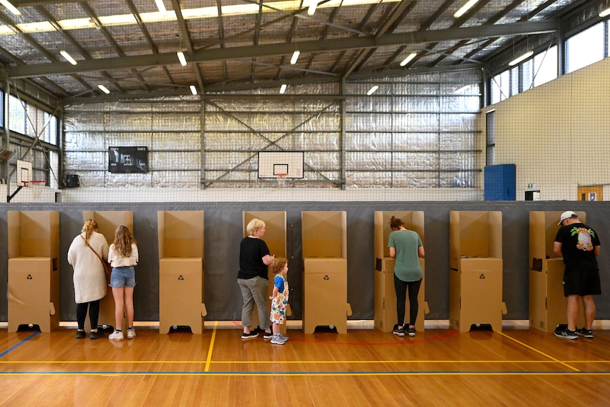 las espaldas de las personas que votan en las urnas instaladas en el salón de una escuela. 