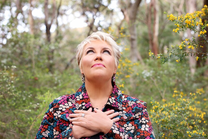 Mid shot of a woman in a floral shirt with hands crossed on her chest looking upwards in a bush setting