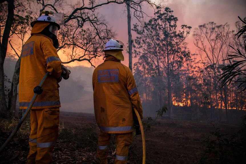 Two firefighters fight a bushfire at Pechey, with the bright glow of flames in front of them.