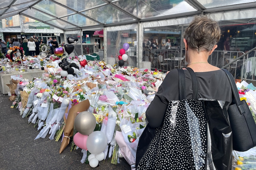 A woman standing near a flower memorial at Bondi Junction.