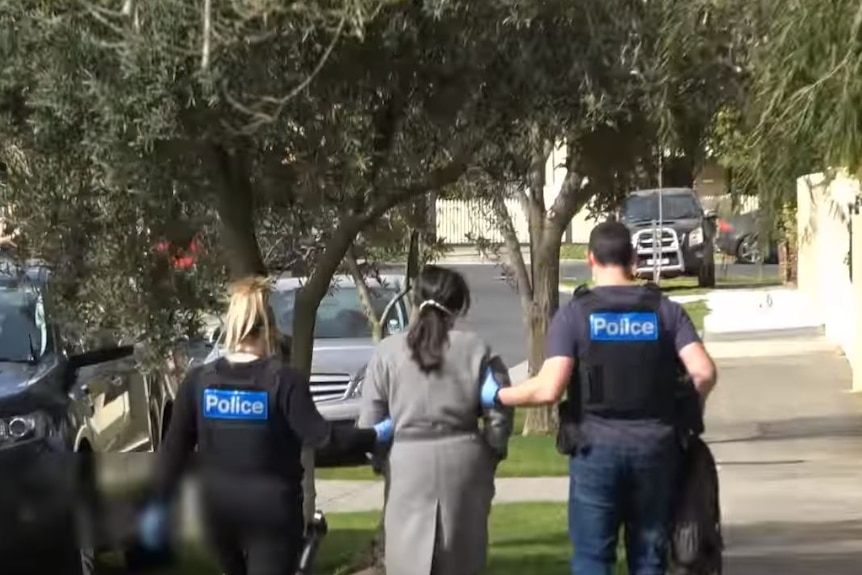 Two police officers escort an unidentified woman away from a property