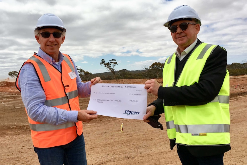 two men in hard hats holding giant cheque on mine site