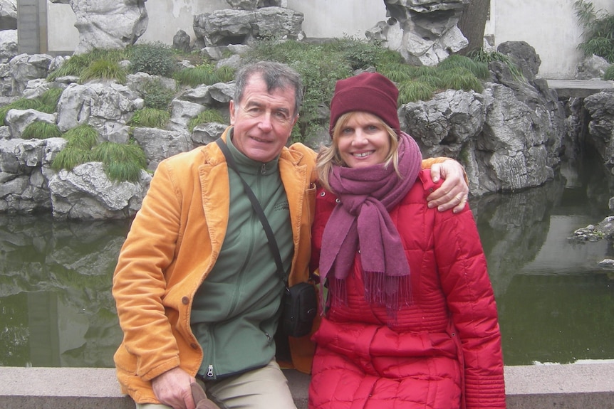 Colour photo of Kerstin Pilz sitting on a wall in the embrace of a man with short brown hair. Both wear bright puffer jackets.
