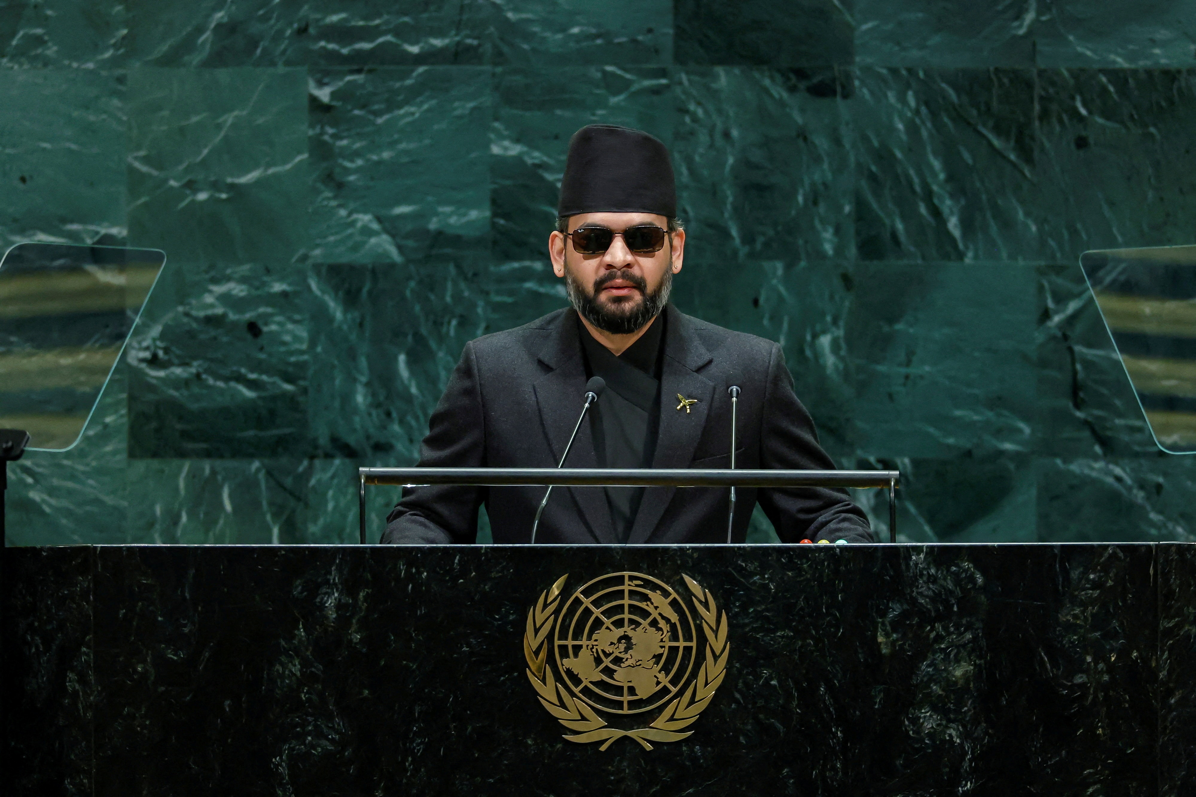 The Prime Minster speaks in black sunglasses in an elegant green stone stage.
