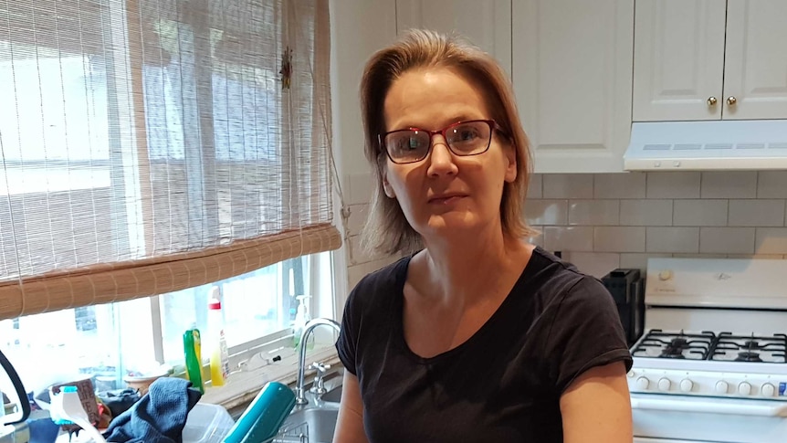 A middle age woman with glasses stands in the middle of a u shaped kitchen