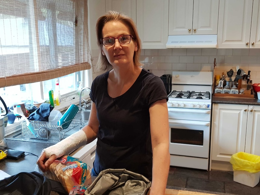 A middle age woman with glasses stands in the middle of a u shaped kitchen