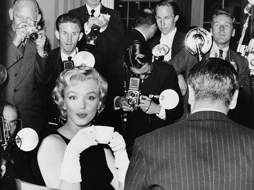 American actress Marilyn Monroe is surrounded by photographers as she sips on a cup of tea at the Savoy Hotel, London.
