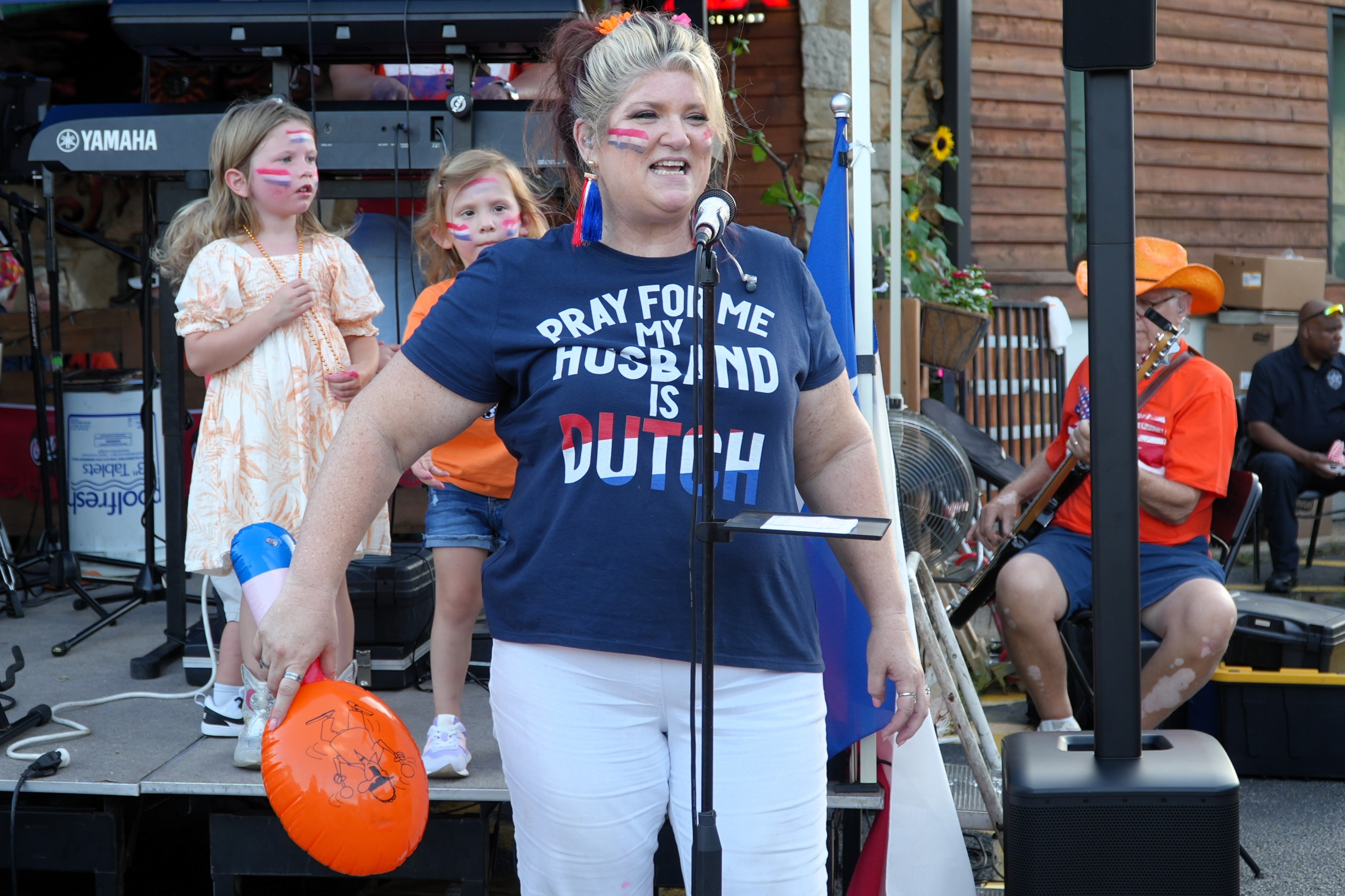 A woman sings into a microphone. She wears a t-shirt saying, "Pray for me, my husband is Dutch".
