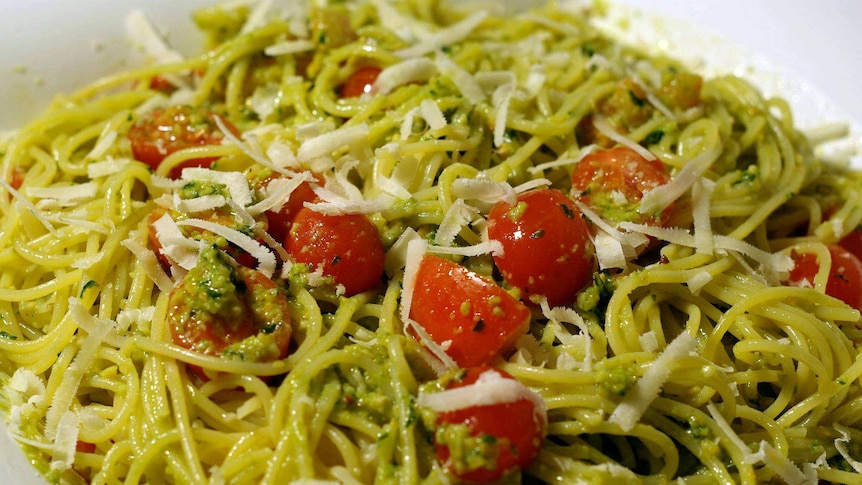 A plate of spaghetti with pesto through, parmesan, tomato and herbs on top.
