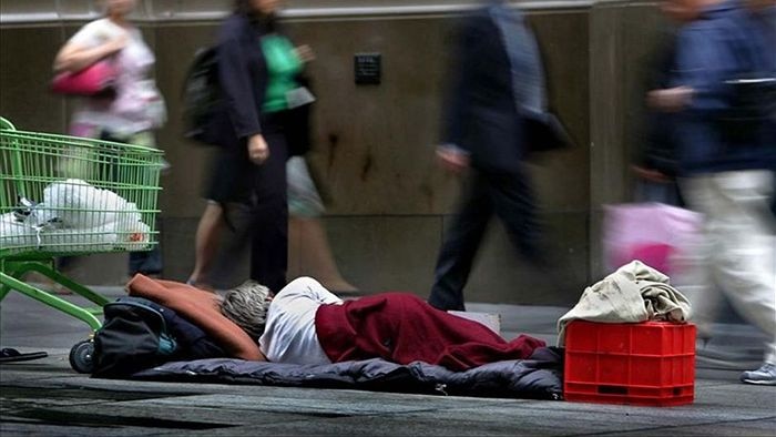 A homeless person lies on the street as business people walk by.
