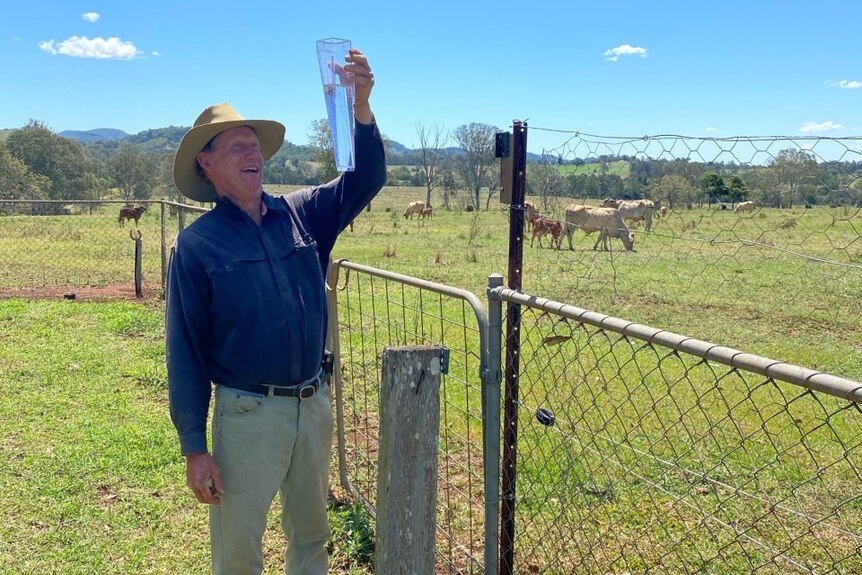 A farmer smiles holding up a rain gauge full of water.